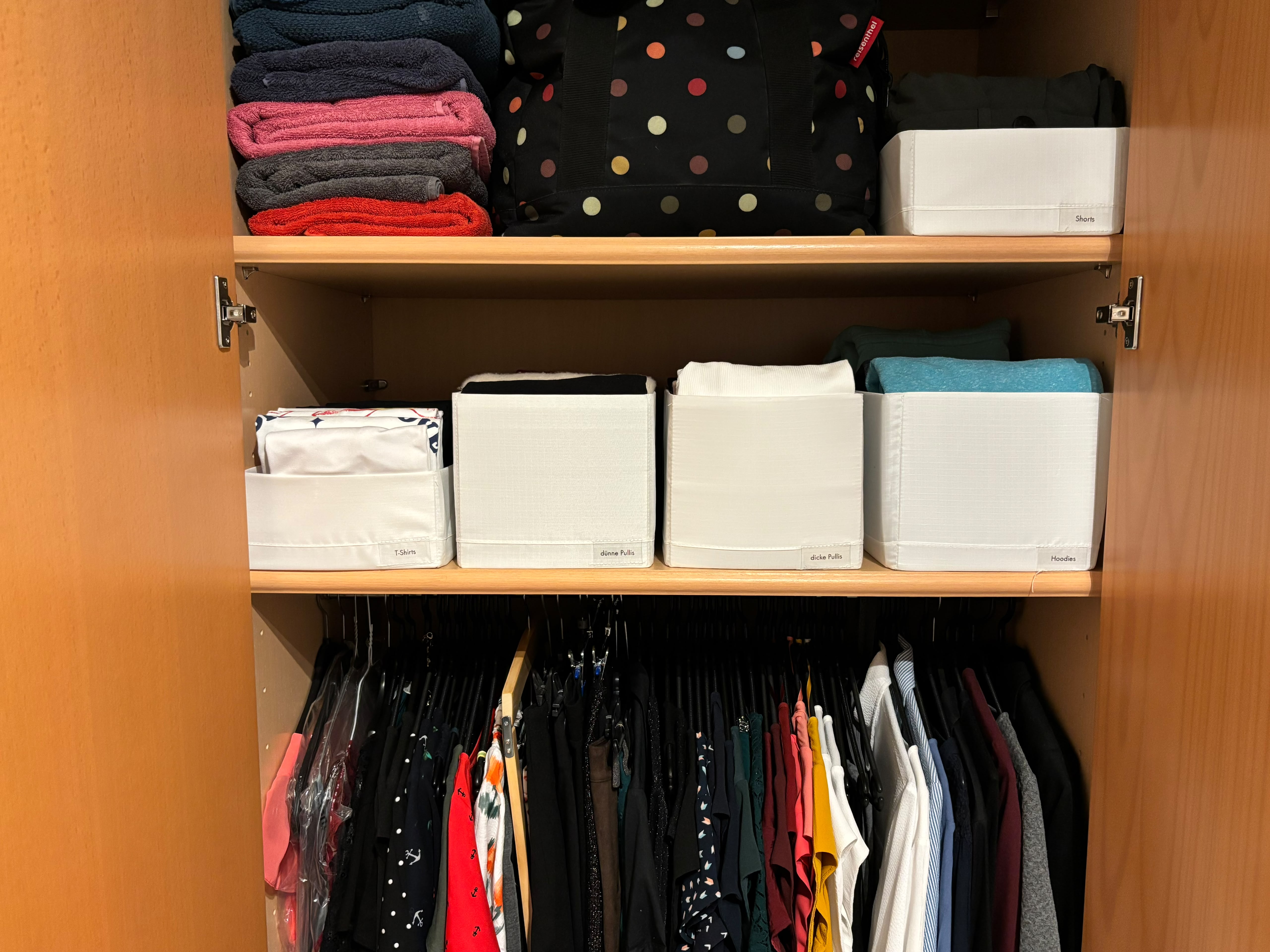 Organisierter Kleiderschrank mit Stange mit Kleidern, Röcken, kurzen und langen Blusen, Stoffhosen, Jäckchen und Blazern